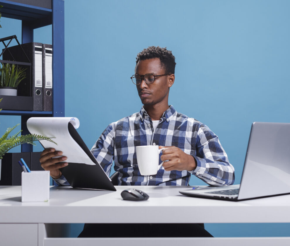 Company office worker having documentation clipboard and coffee cup looking over project management charts.