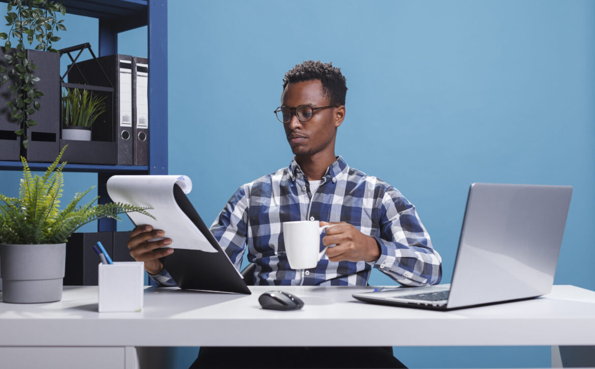 Company office worker having documentation clipboard and coffee cup looking over project management charts.