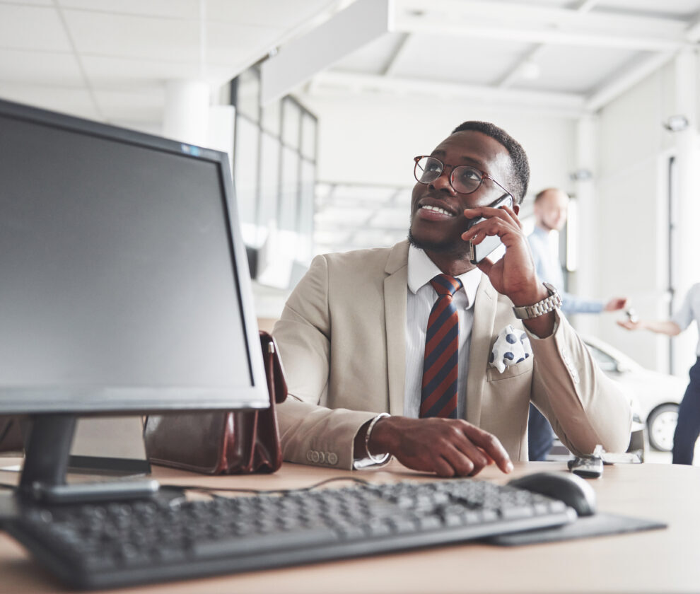 Attractive black businessman sits at the table at the car dealership, he signs a contract and buys a new car