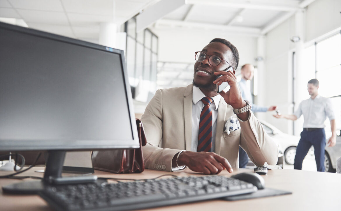 Attractive black businessman sits at the table at the car dealership, he signs a contract and buys a new car